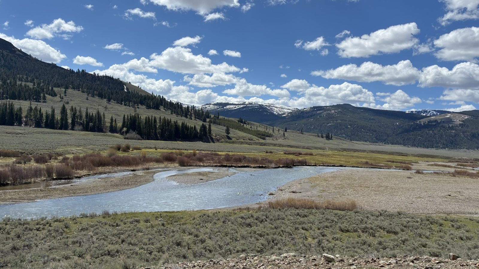 Shallow river winding through a sagebrush valley below forested hills and snowy peaks in Montana